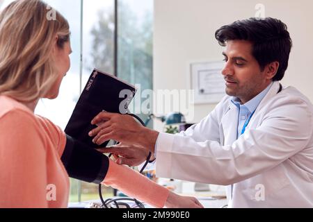 Male Doctor Or GP Examining Mature Female Patient Taking Blood Pressure With Sphygmomanometer Stock Photo