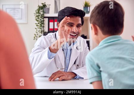 Doctor Or GP In White Coat Meeting Mother And Son For Appointment Giving Boy High Five Stock Photo