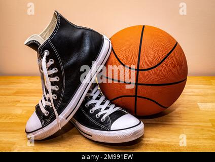 Basketball and pair of classic leather basketball shoes on hardwood floor. Stock Photo
