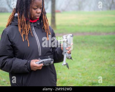 Cheerful young teenager african american wearing sportswear checking flying a camera drone in a park before use. Stock Photo