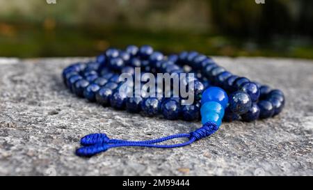 Blue buddhist mala prayer beads (lapislazuli) on stone, close up. Mindfulness and japa meditation accessory. Stock Photo