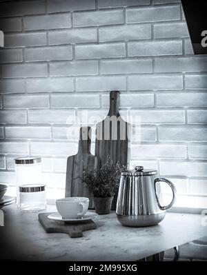 A still life with a teapot, cup, cutting boards, and some jars in black and white Stock Photo