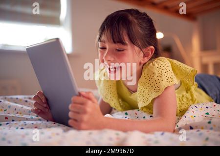 Girl In Bedroom Lying On Bed Enjoying Using Digital Tablet Stock Photo