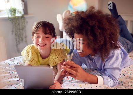 Girl And Boy In Bedroom Lying On Bed Using Digital Tablet Together Stock Photo