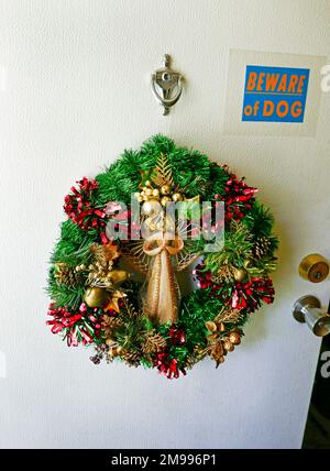 Christmas wreath hangs on front door of home alongside dog warning sign. Stock Photo