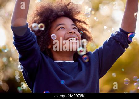 Smiling Boy Outdoors Having Fun Playing With Bubbles In Garden Stock Photo