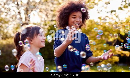 Smiling Boy And Girl Outdoors Having Fun Playing With Bubbles In Garden Stock Photo