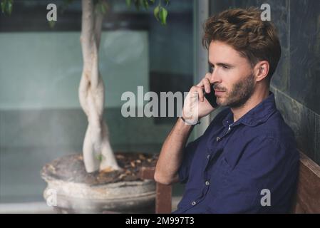 Young man talking on the phone outside of an educational building. Stock Photo