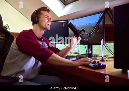 Man Gaming At Home Wearing Wireless Headphones Sitting At Desk With Multiple Monitors Stock Photo