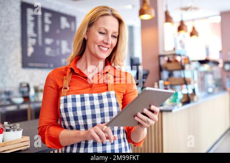 Mature Female Owner Of Coffee Shop Or Restaurant Using Digital Tablet Stock Photo