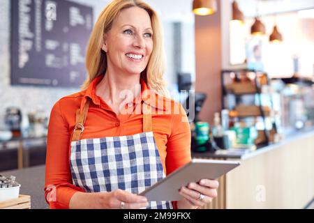Mature Female Owner Of Coffee Shop Or Restaurant Using Digital Tablet Stock Photo