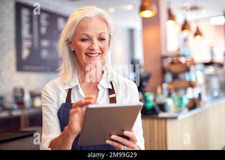 Mature Female Owner Of Coffee Shop Or Restaurant Using Digital Tablet Stock Photo