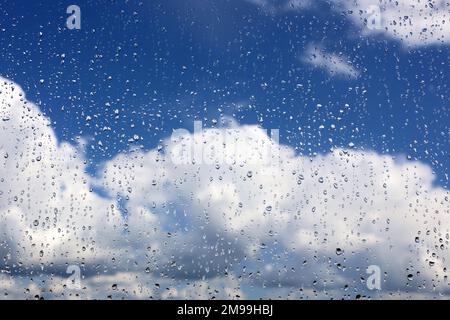 Raindrops on the window glass on blurred background of sky with white clouds. Beautiful water drops, weather after rain Stock Photo