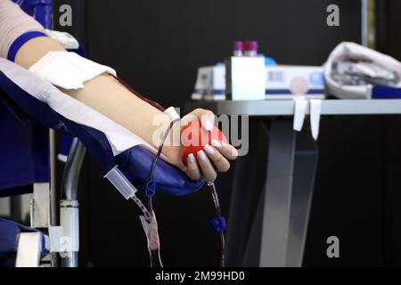 Woman blood donor in chair during donation with a blood bag and red bouncy ball in hand, selective focus. Concept of donorship, transfusion Stock Photo