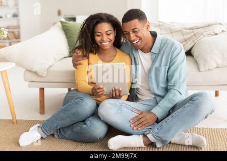 Happy laughing young african american couple hugging looking at tablet webcam, watch funny video Stock Photo