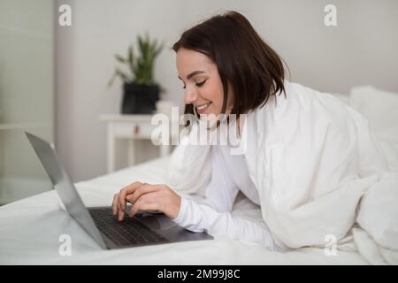 Relaxed young woman chilling in bed with modern laptop Stock Photo