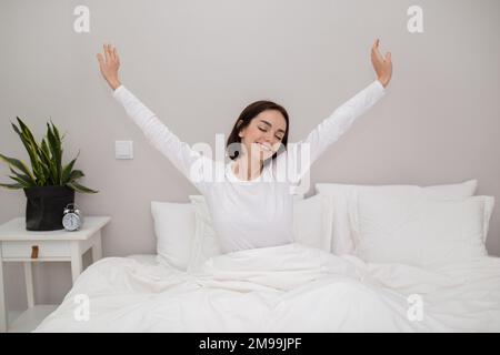 Smiling young woman enjoying happy morning, stretching in bed Stock Photo
