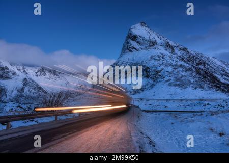 Snowy mountains and blurred car headlights on the road in winter Stock Photo
