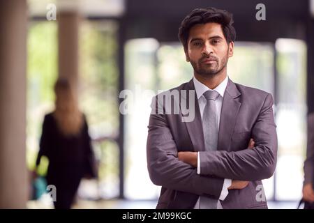Portrait Of Businessman Standing In Lobby Of Busy Modern Office Building Stock Photo