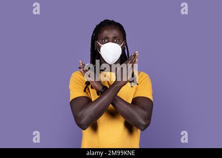 Black guy in protective medical mask gesturing stop on purple Stock Photo