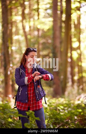 Woman On Holiday Hiking Through Woods Using GPS App On Smart Watch To Navigate Stock Photo