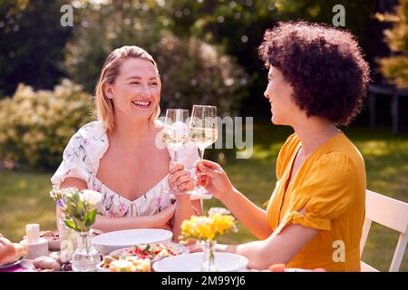 Two Female Friends Sitting Outdoors In Summer Garden At Home Drinking Wine And Eating Meal Stock Photo