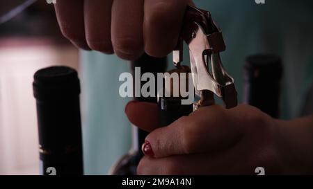 Man opens bottle of wine in dark room, two empty bottles in background. Stock Photo