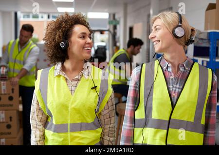 Two Female Workers Using Headsets In Distribution Warehouse Stock Photo
