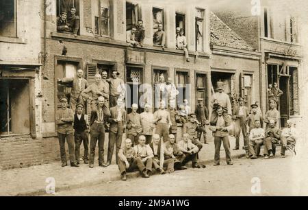 A fascinaing WW1-era postcard showing a large group of German soldiers posed in the setting of a battle-scarred street scene in France (note the sign 'Restaurant Jeanne D'Arc' - number 19). Whether they are captured prisoners of war or relaxing behind the lines (in occupied territory) is not known. Many of the soldiers have fully shaven or very close-cropped haircuts. Stock Photo