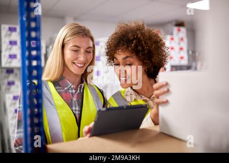 Two Female Workers In Logistics Distribution Warehouse Using Digital Tablet Stock Photo