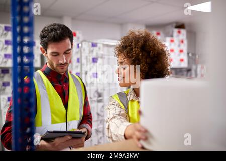 Male And Female Workers In Logistics Distribution Warehouse Using Digital Tablet Stock Photo