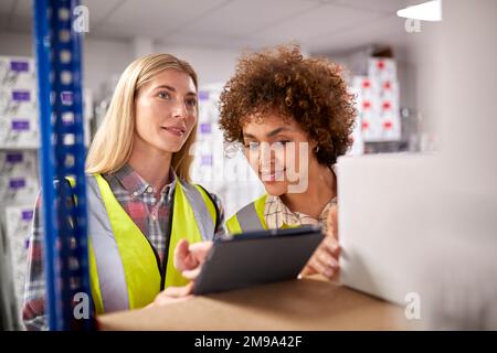 Two Female Workers In Logistics Distribution Warehouse Using Digital Tablet Stock Photo