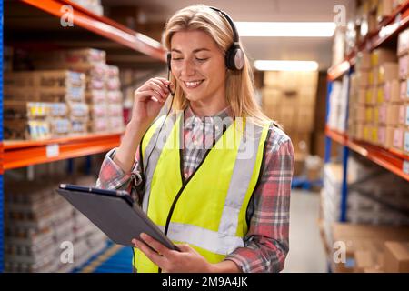 Female Worker Wearing Headset In Logistics Distribution Warehouse Using Digital Tablet Stock Photo
