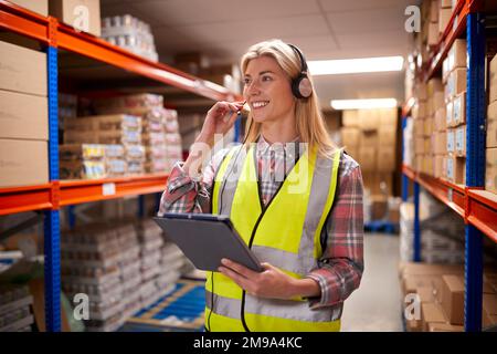 Female Worker Wearing Headset In Logistics Distribution Warehouse Using Digital Tablet Stock Photo