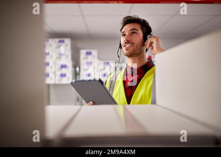 Male Worker Wearing Headset In Logistics Distribution Warehouse Using Digital Tablet Stock Photo