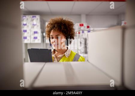 Female Worker Wearing Headset In Logistics Distribution Warehouse With Digital Tablet Stock Photo