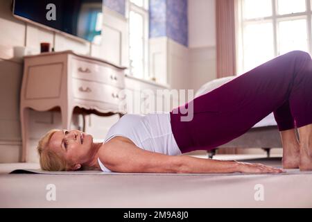 Active Mature Woman Exercising Doing Yoga On Mat At Home Stock Photo