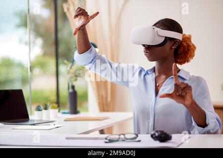 Woman Working From Home Office Sitting At Desk Wearing VR Headset Interacting With AR Technology Stock Photo