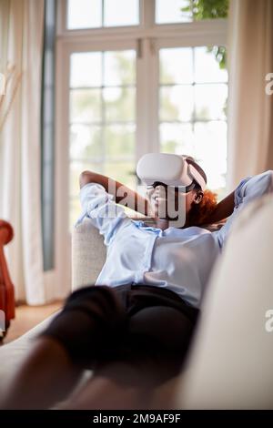 Woman Relaxing Lying On Sofa At Home Wearing VR Headset And Interacting With AR Technology Stock Photo