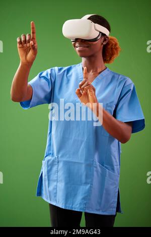 Female Nurse Or Doctor In Scrubs With VR Headset Interacting With AR Technology Against Green Screen Stock Photo