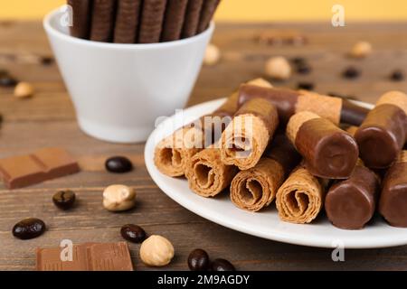 Plate of delicious wafer rolls with hazelnuts, coffee beans and chocolate pieces on wooden table Stock Photo