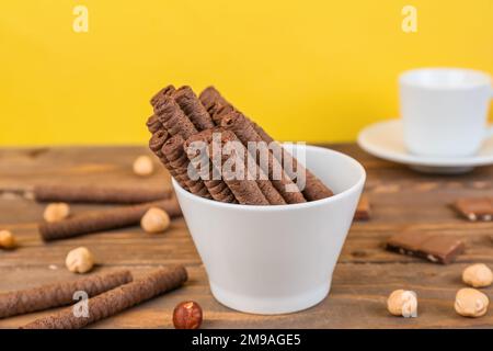Tasty rolled wafer cookies with hazelnuts and chocolate pieces on wooden table Stock Photo