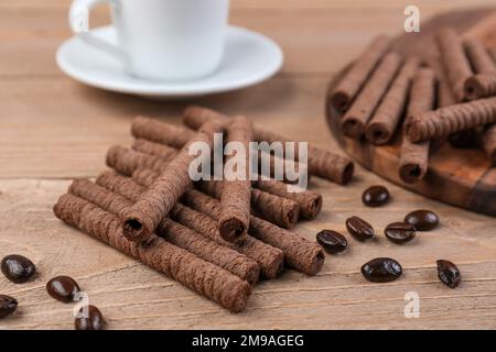 Tray with tasty rolled wafer cookies, coffee beans and cup on wooden background Stock Photo