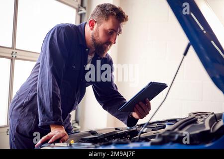 Male Mechanic In Garage Using Diagnostic Software On Digital Tablet To Service Car Engine Stock Photo