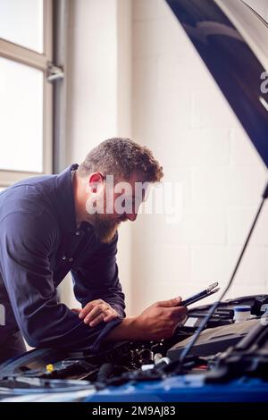 Male Mechanic In Garage Using Diagnostic Software On Digital Tablet To Service Car Engine Stock Photo