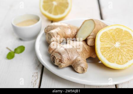 Plate with fresh ginger roots, powder and lemon on wooden table, closeup Stock Photo