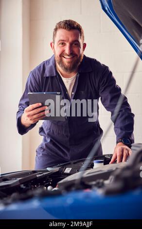 Portrait Of Male Mechanic In Garage Using Diagnostic Software On Digital Tablet To Service Car Stock Photo