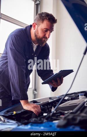 Male Mechanic In Garage Using Diagnostic Software On Digital Tablet To Service Car Engine Stock Photo