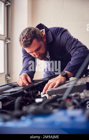 Male Mechanic In Garage Looking Under Hood Of Car Whilst Servicing Engine Stock Photo