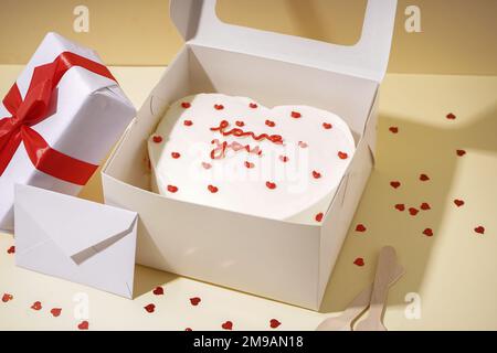 Opened box with tasty bento cake, gift and envelope on beige table. Valentine's Day celebration Stock Photo
